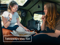 Two women sitting inside a TentBox with takeaways, featuring the TentBox CoolBag and text reading 'takeaways stay hot'.