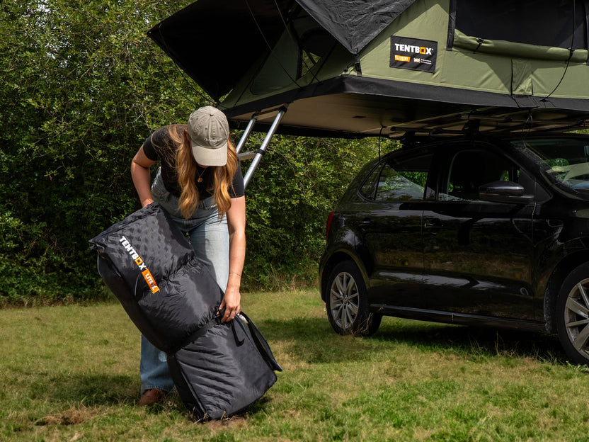 User packing the TentBox Lite XL Mattress Topper into storage bag under open rooftop tent – portable and travel-ready